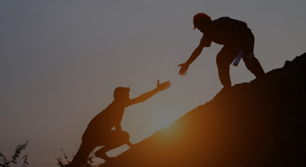 Silhouette of one climber reaching down to pull another up a hillside