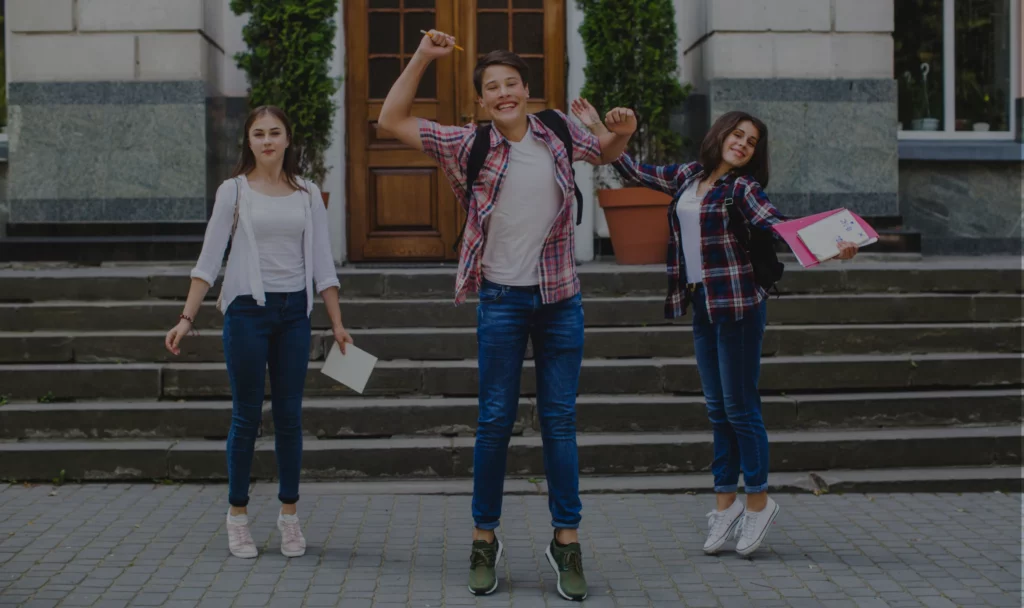 Three students celebrating on the steps of a school building