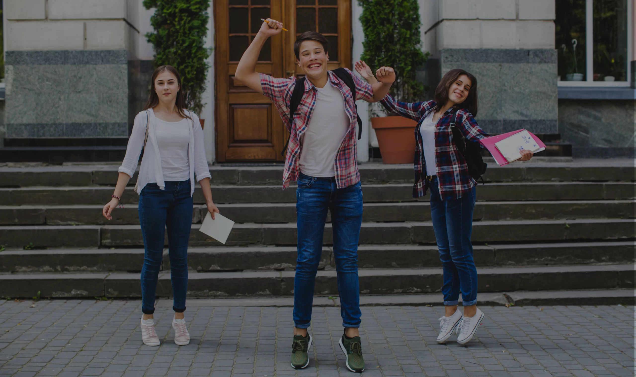 Three students jumping with joy on the steps of a school