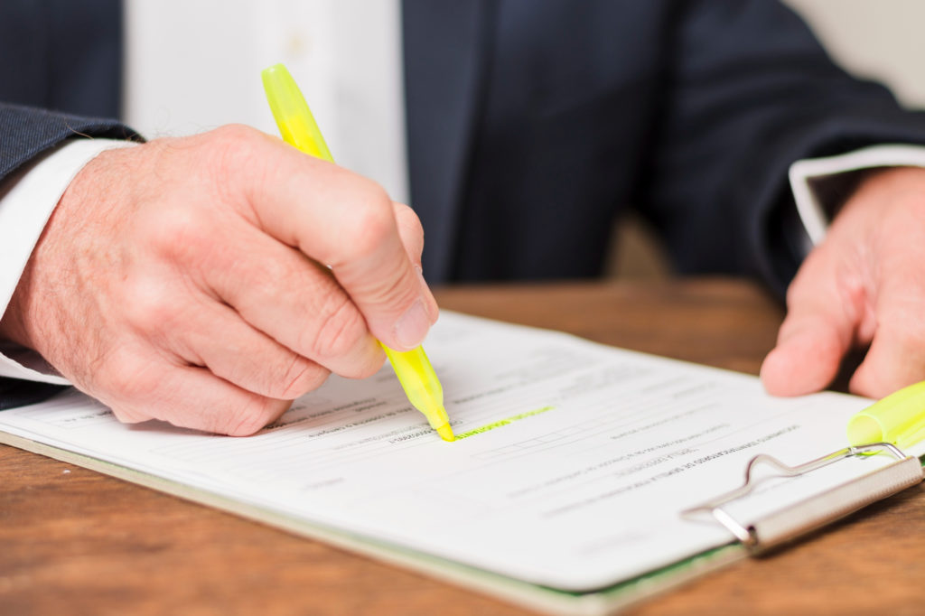 A hand marking a document with a yellow highlighter