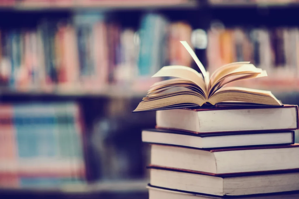An open book on a stack of books in front of library shelves